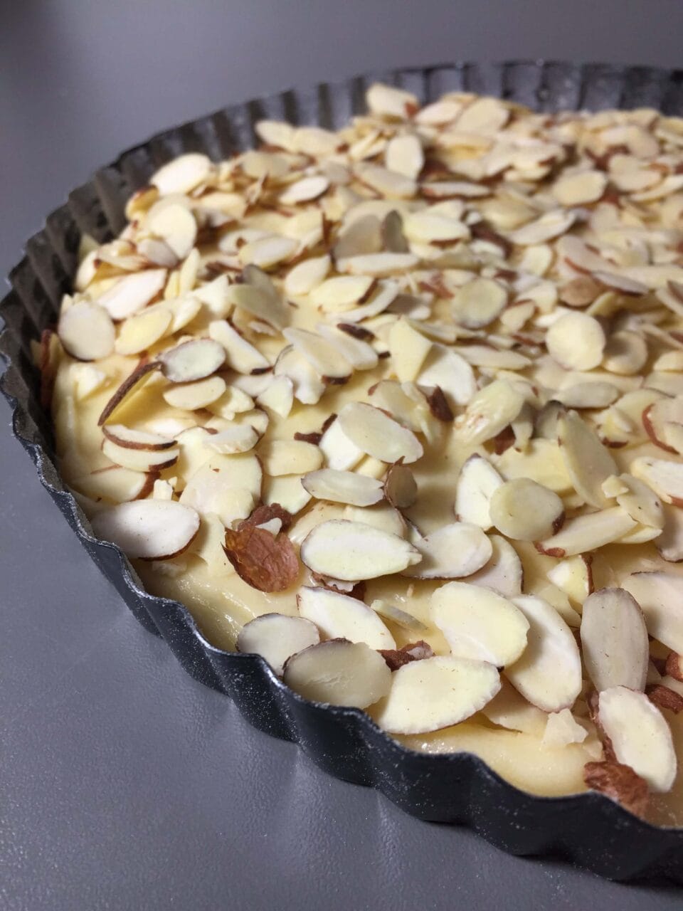 Cake batter topped with sliced almonds in a fluted baking pan, ready to be baked.