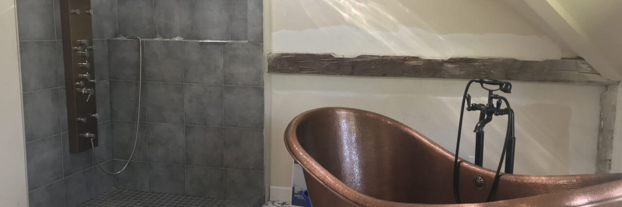 A bathroom with a freestanding copper bathtub and a gray tiled walk-in shower.